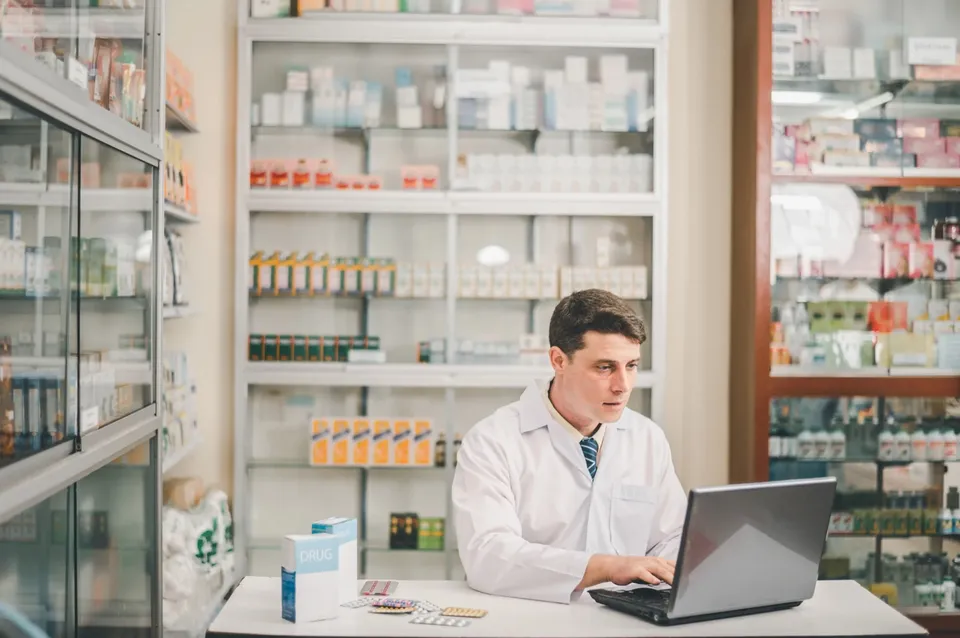 Pharmacist reviewing claims on a laptop at the pharmacy counter
