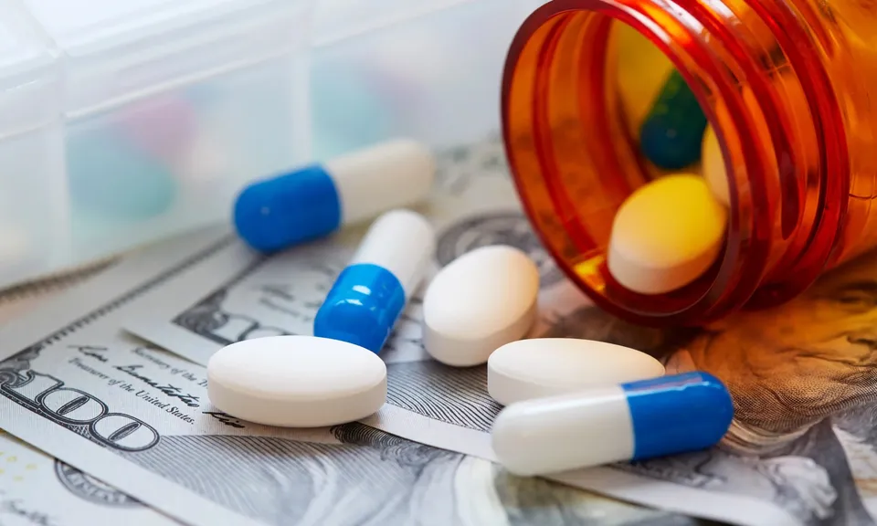Prescription capsules spilling from a pill bottle onto U.S. currency